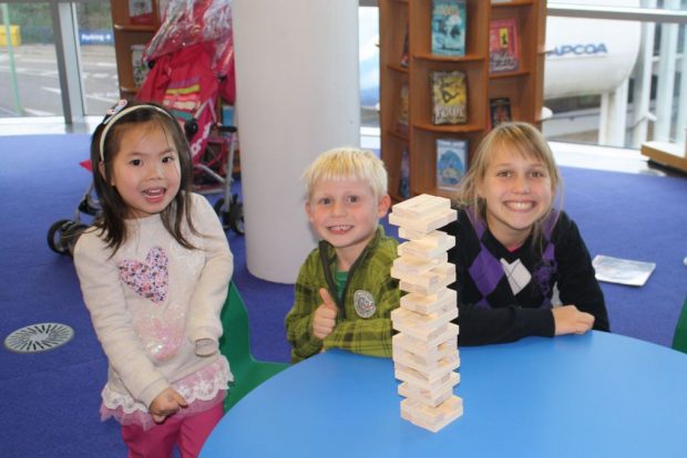 Photo of 3 children playing Jenga in a library.