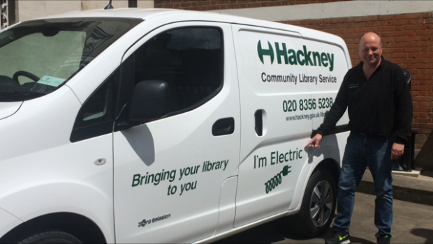 A photo of a man standing beside a new small white van which says 'I'm electric' on the side