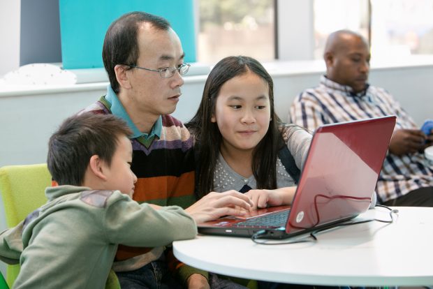 Photo of a family sitting around a laptop in a library.