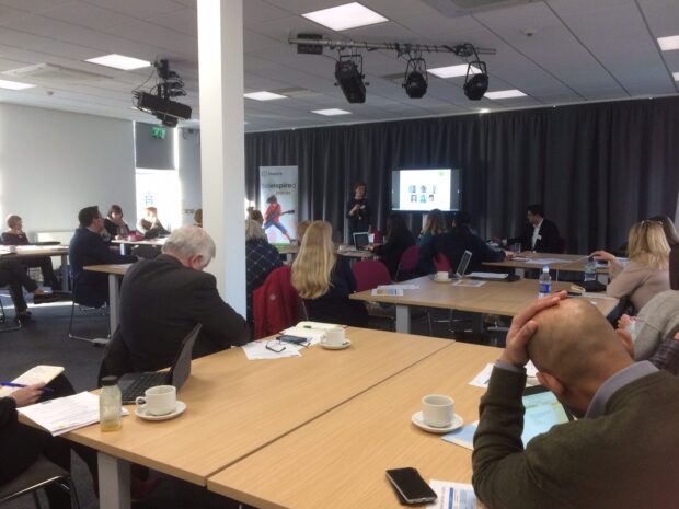 Photo of a group of people sitting around tables watching a presentation