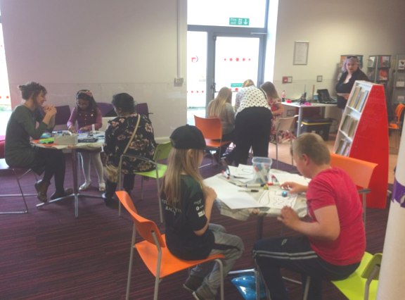 Photo of people sitting at tables and doing different digital activities.