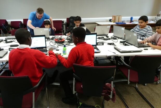 Photo of a group of young people sitting around a table and working on laptops