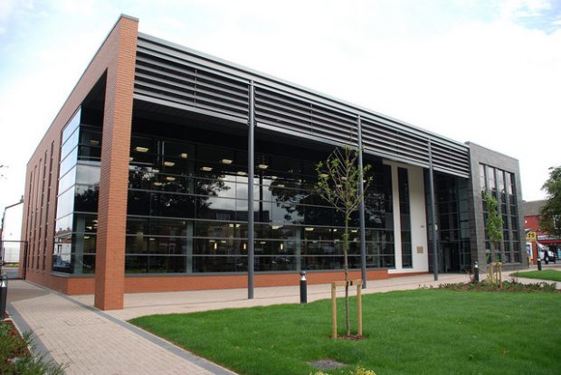 Photo of the outside of a modern library, the front wall is all glass.