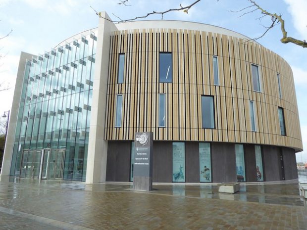 Photo of the outside of a new library with high glass windows and wood cladding.