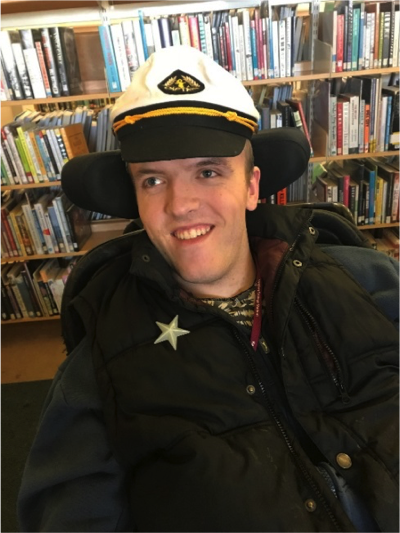 Photo of a young man in a wheelchair with a sailors cap on.