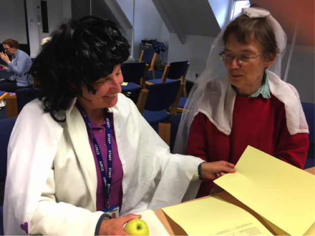 Photo of 2 women dressing up and looking at information sheets.