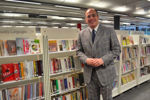 Photo of a man in a grey suit in front of bookcases in a library.