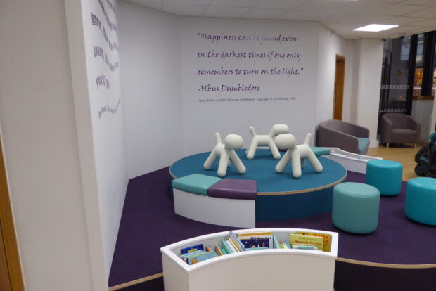 Photo of a corner in the library where there is a small platform and colourful stools