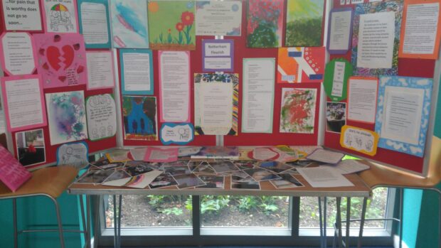 Photo of a table with photos on and 3 display boards with art work and poems on them.