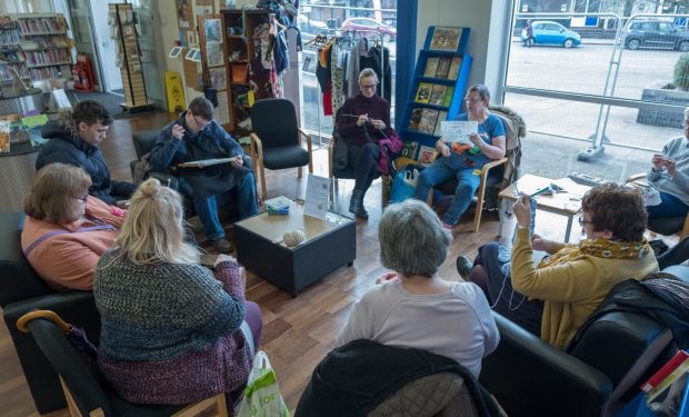 A group of people sitting knitting in a library