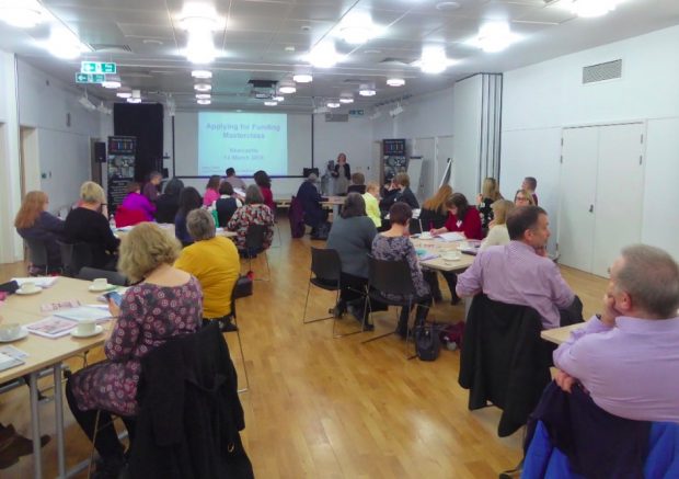 Photo of people sitting around tables watching a presentation