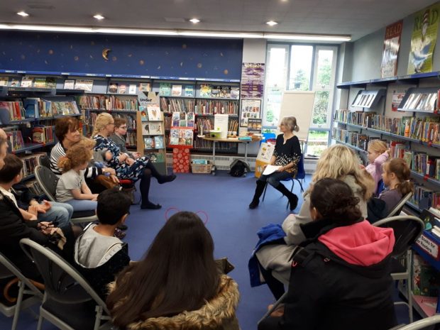 Photo of Helen Moss in Loughton library talking to a group of people sitting around her on chairs.