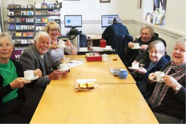 Photo of people sitting around a table drinking tea and coffee.