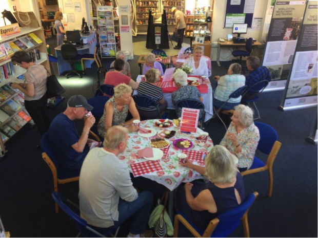 Photo of people sitting around 2 tables eating cake and talking.