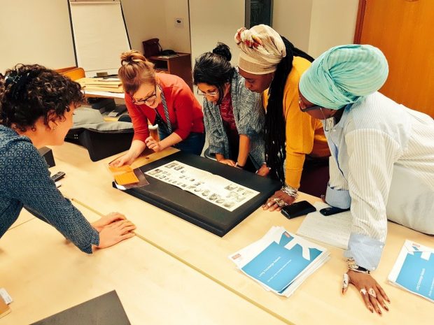 Photo of 5 women standing around a table looking at an archive item.