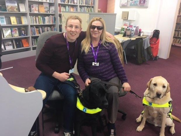 Photo of 2 volunteers with their guide dogs in the library