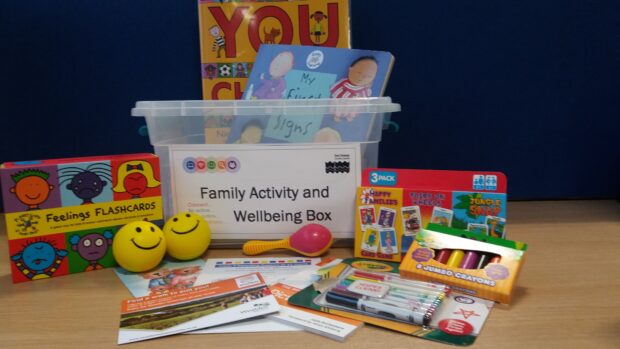 Photo of a family activity and wellbeing box which contains Feelings Flashcards, balls, books and colouring pens