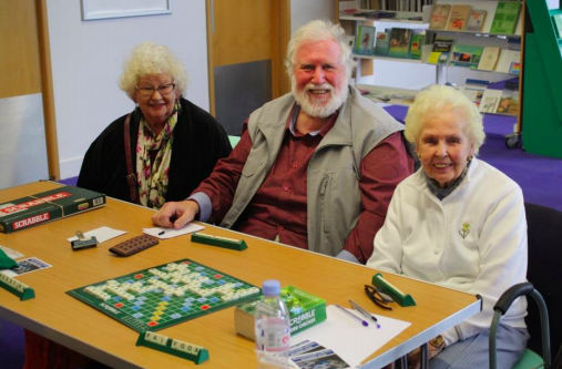 Photo of 3 elderly people playing scrabble in a library