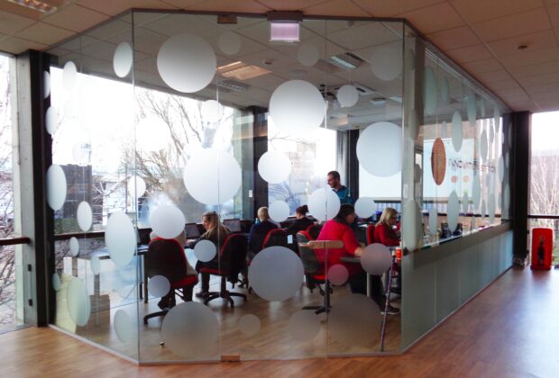 Photo of Stockton’s Innovation Station. A room with glass walls and people sitting inside it at desks.