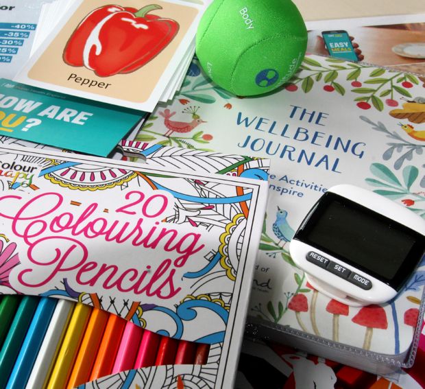 Photo of some of the contents of a wellbeing box including 20 colouring pencils, a squidgy ball, a step counter and a wellbeing journal