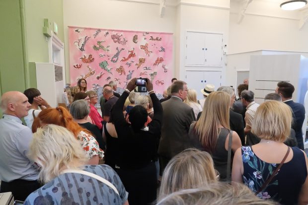 Photo of a room full of people with a large mural with people flying over the town of Hastings