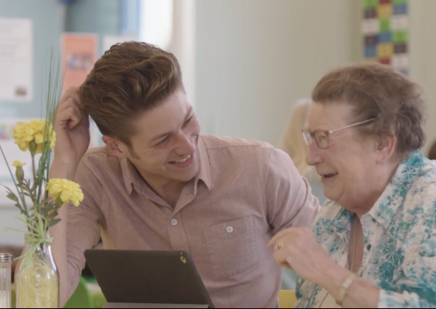 Photo of an elderly lady being shown how to use a computer by a young man