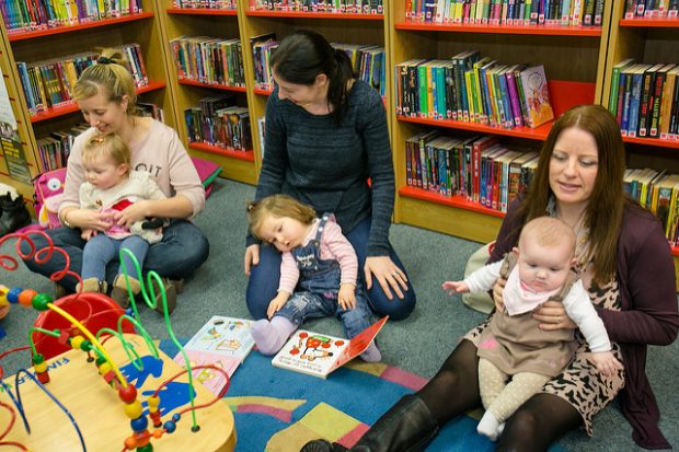 Photo of 3 women and their babies sitting on the floor of a library