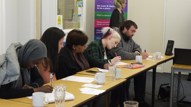 A row of people sitting at a desk in a classroom situation