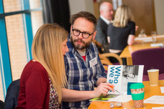 Photo of a female customer sitting next to a man who is pointing at a booklet, offering advice (he is wearing a badge which marks him as an official adviser)