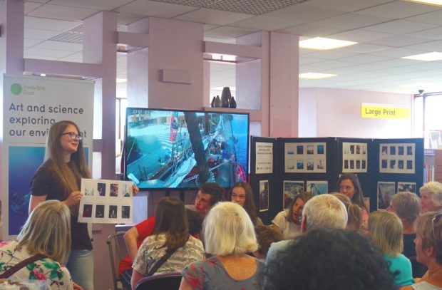 Photo of a woman giving a presentation in front of an audience in a library