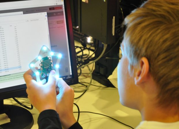 Photo of a young boy sitting in front of a computer screen, holding a micro:bit computer, wich is surrponded by bright lights in the shape of a star