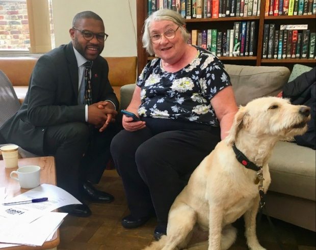 Man and older woman sitting in a library, her guide dog at her feet