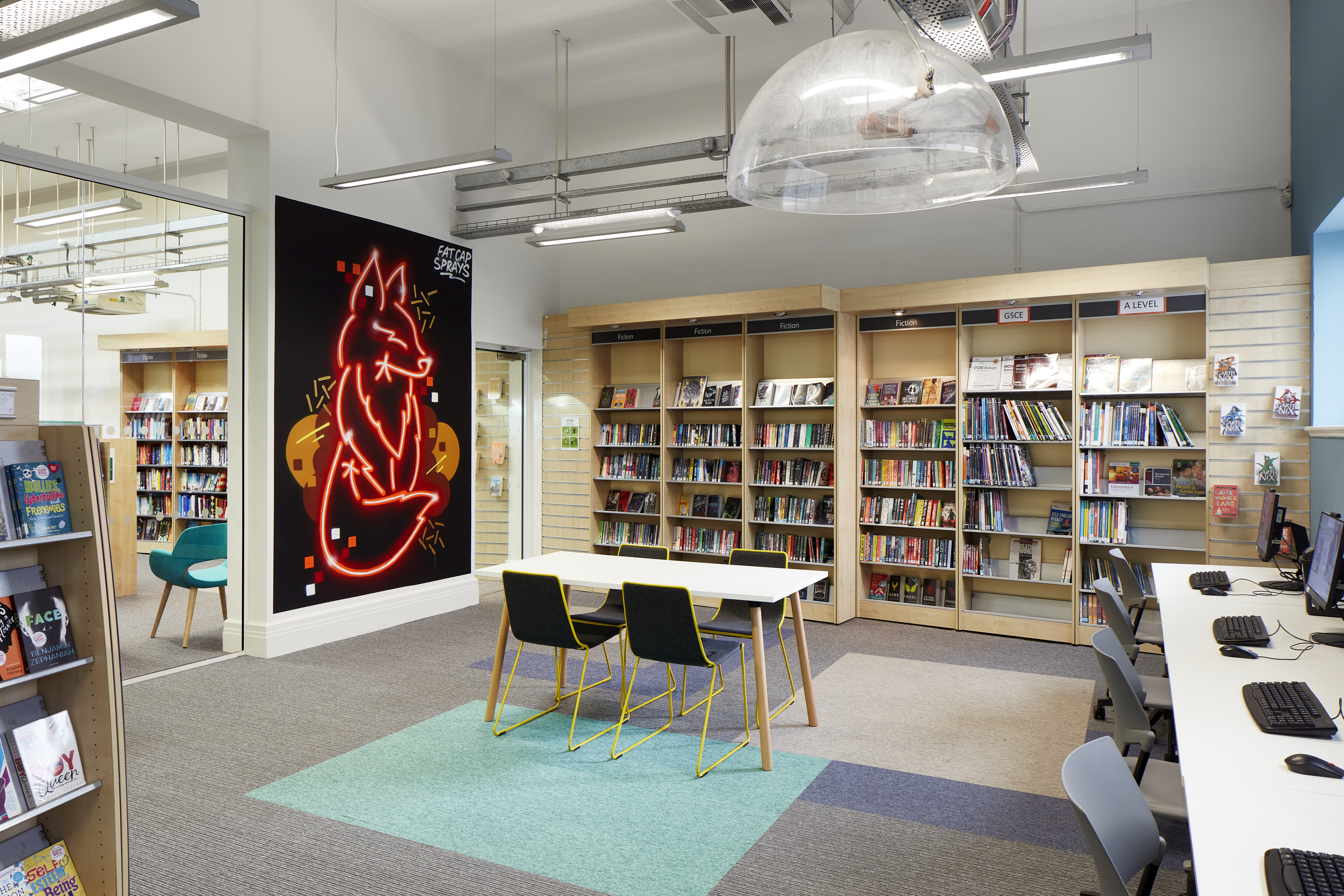 Internal shot of Eltham library, showing bookshelves, a table with chairs and art work on the wall
