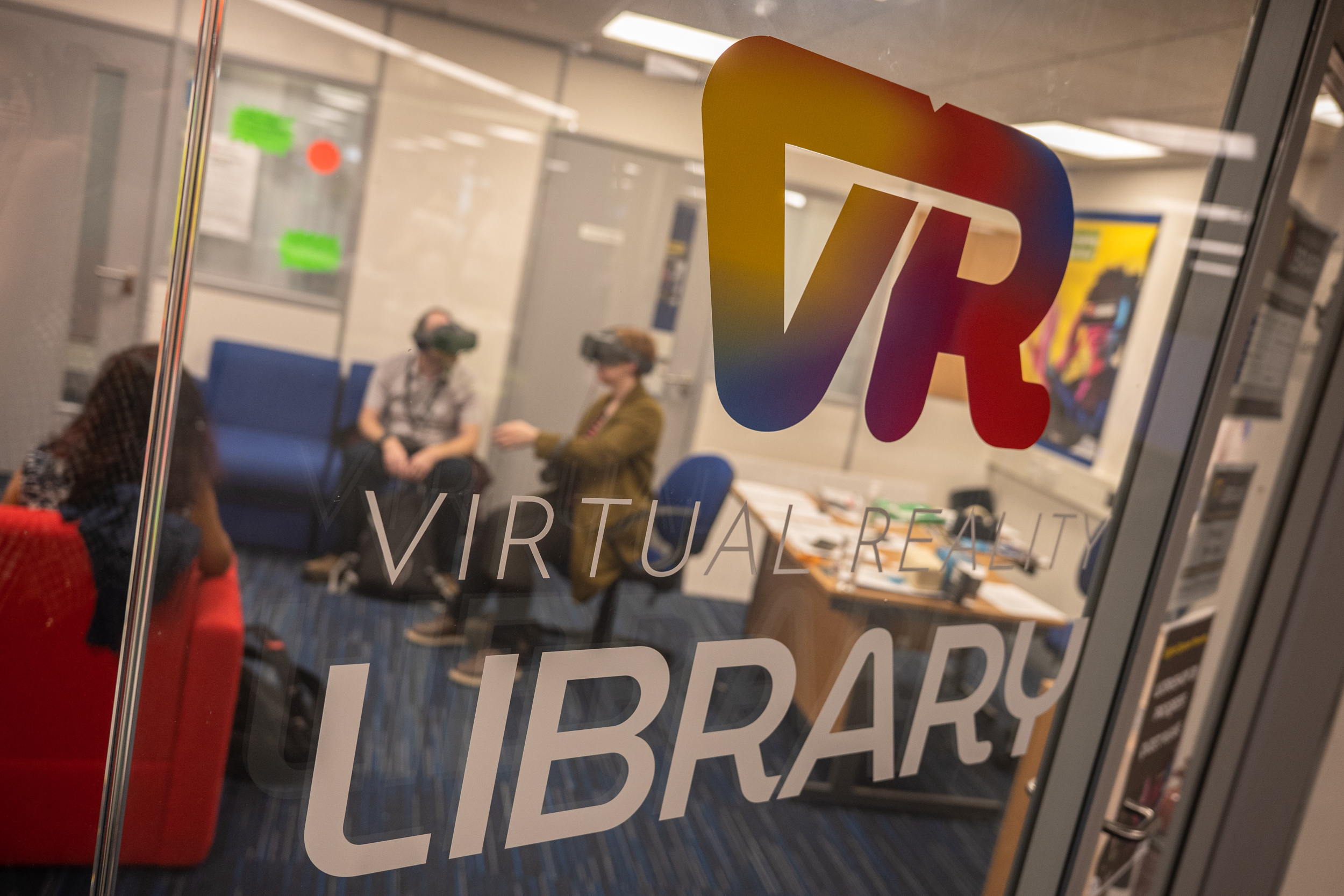 Image showing class screen with sign saying 'VR virtual library' with two people seated behind