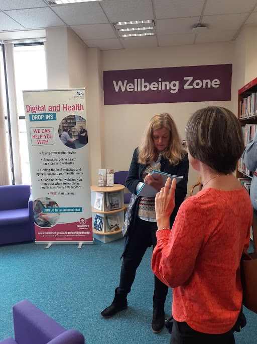 Baroness Sanderson and a member of library staff in front of Wellbeing Zone signage at Yeovil Library